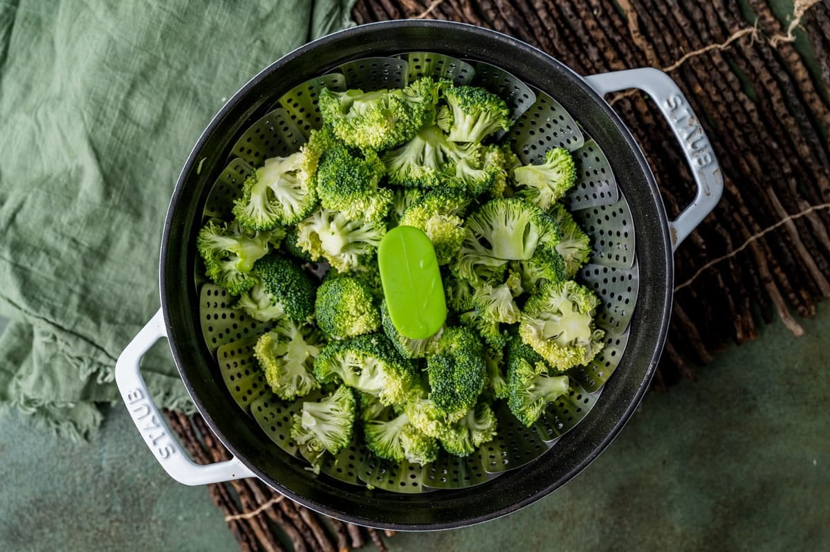 fresh broccoli in a steamer basket in a staub pan