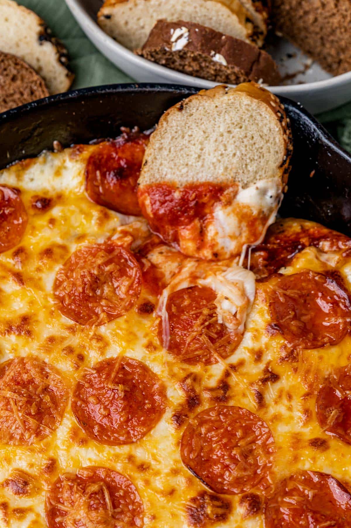 a piece of Italian bread in a skillet of hot cheese dip
