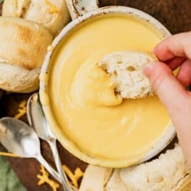 a hand holding bread dipping in cheese fondue