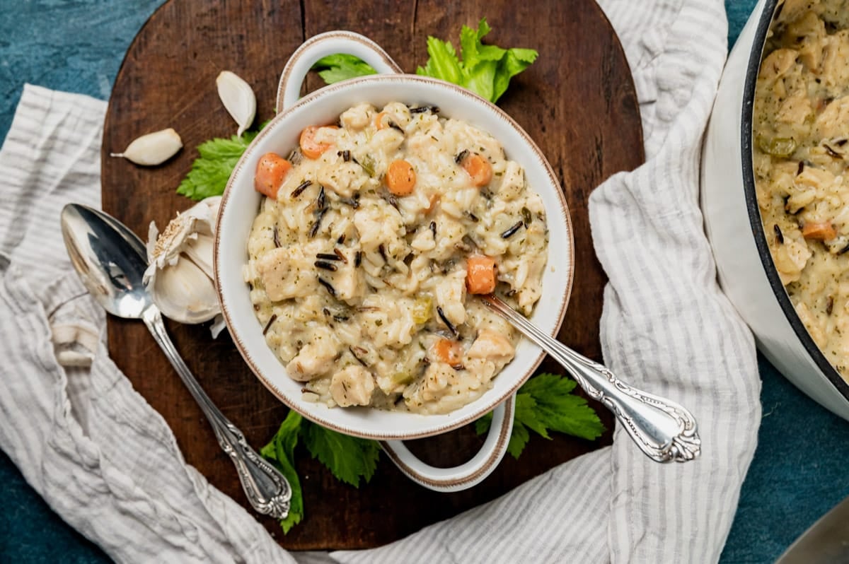 a bowl of chicken and wild rice soup on a cutting board