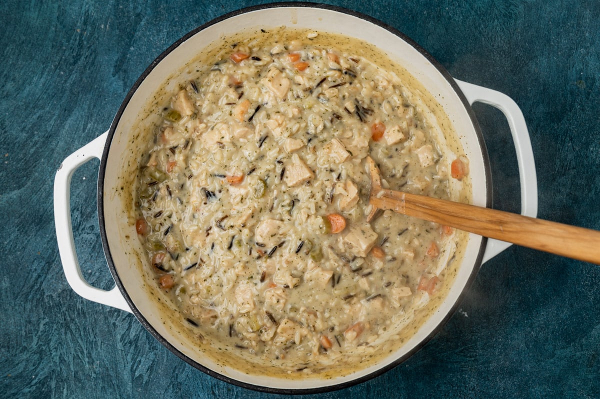 chicken & wild rice soup in a dutch oven with a wooden spoon