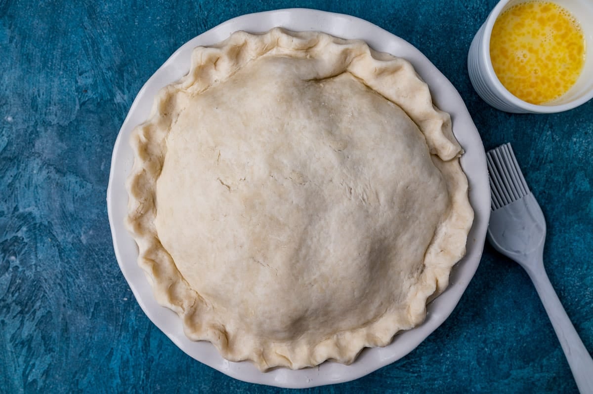 an unbaked pie sitting on a table with a pastry brush and egg