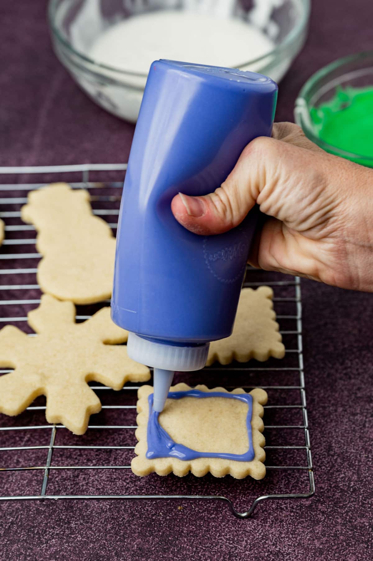 squeezing sugar cookie icing on a cut out cookie