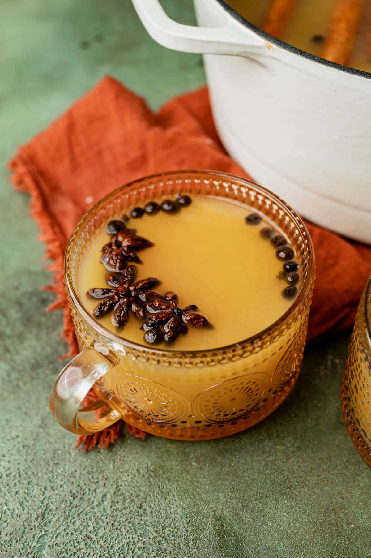 a cup of mulled apple cider with allspice and star anise on top