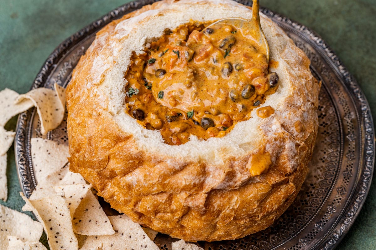 spoon ladling cheesy sausage dip in a bread bowl