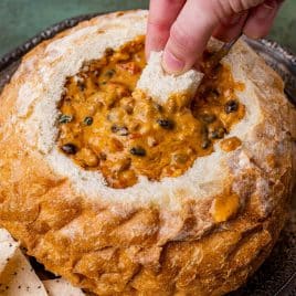 dipping bread in cheesy sausage dip in a bread bowl