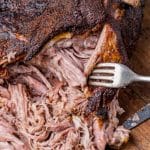 a fork tearing into a cooked pork shoulder on a cutting board