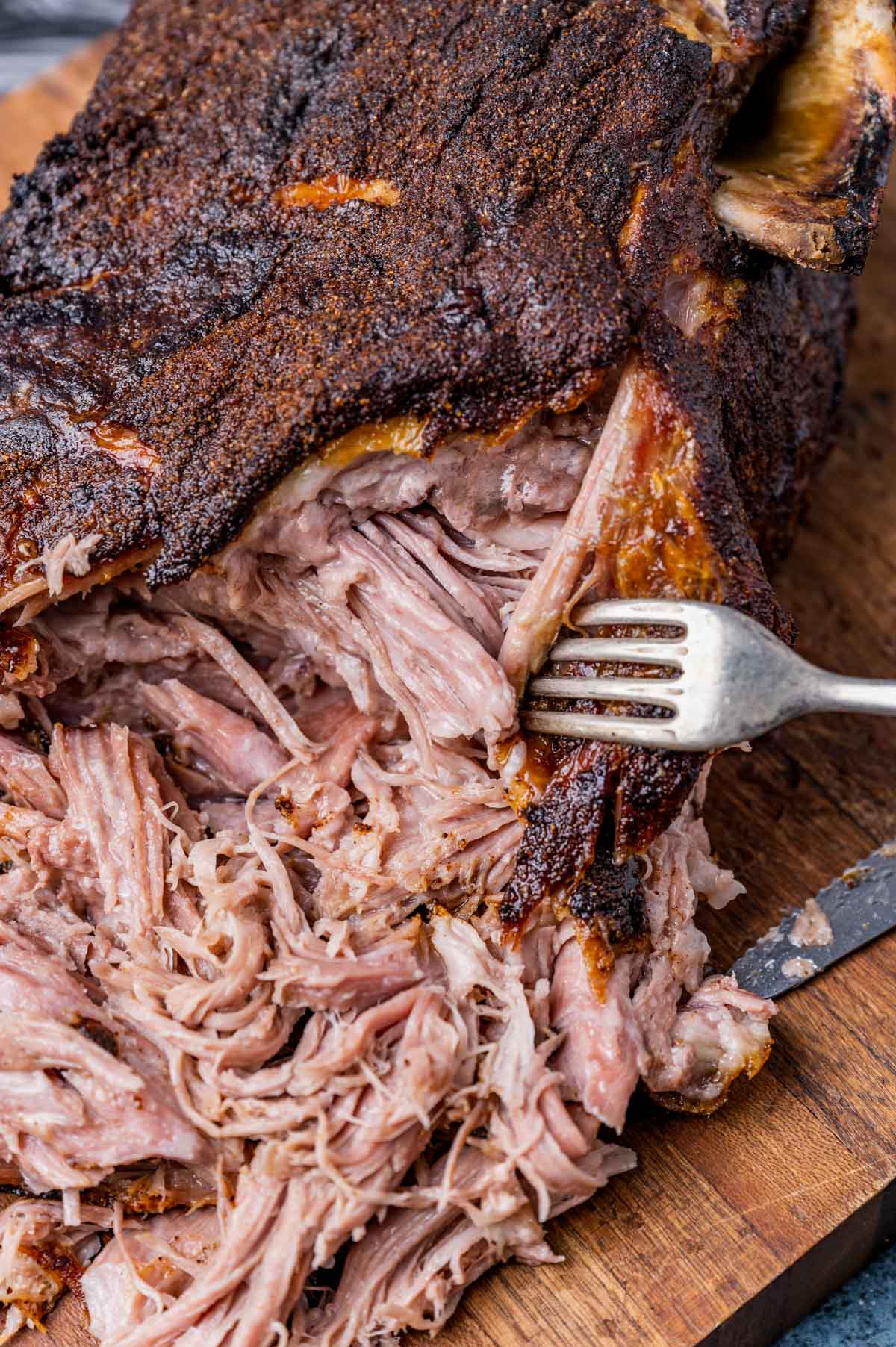 a fork tearing into a cooked pork shoulder on a cutting board