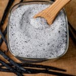 a square glass container of vanilla sugar with a measuring teaspoon in it