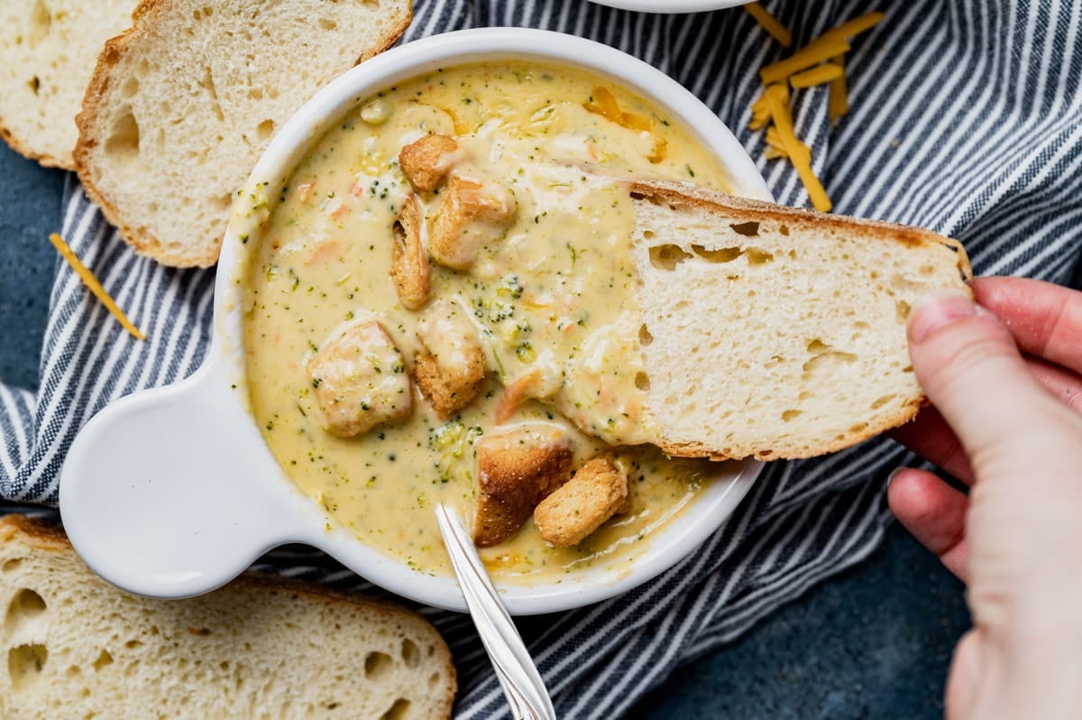 a piece of bread dipping into broccoli cheddar soup