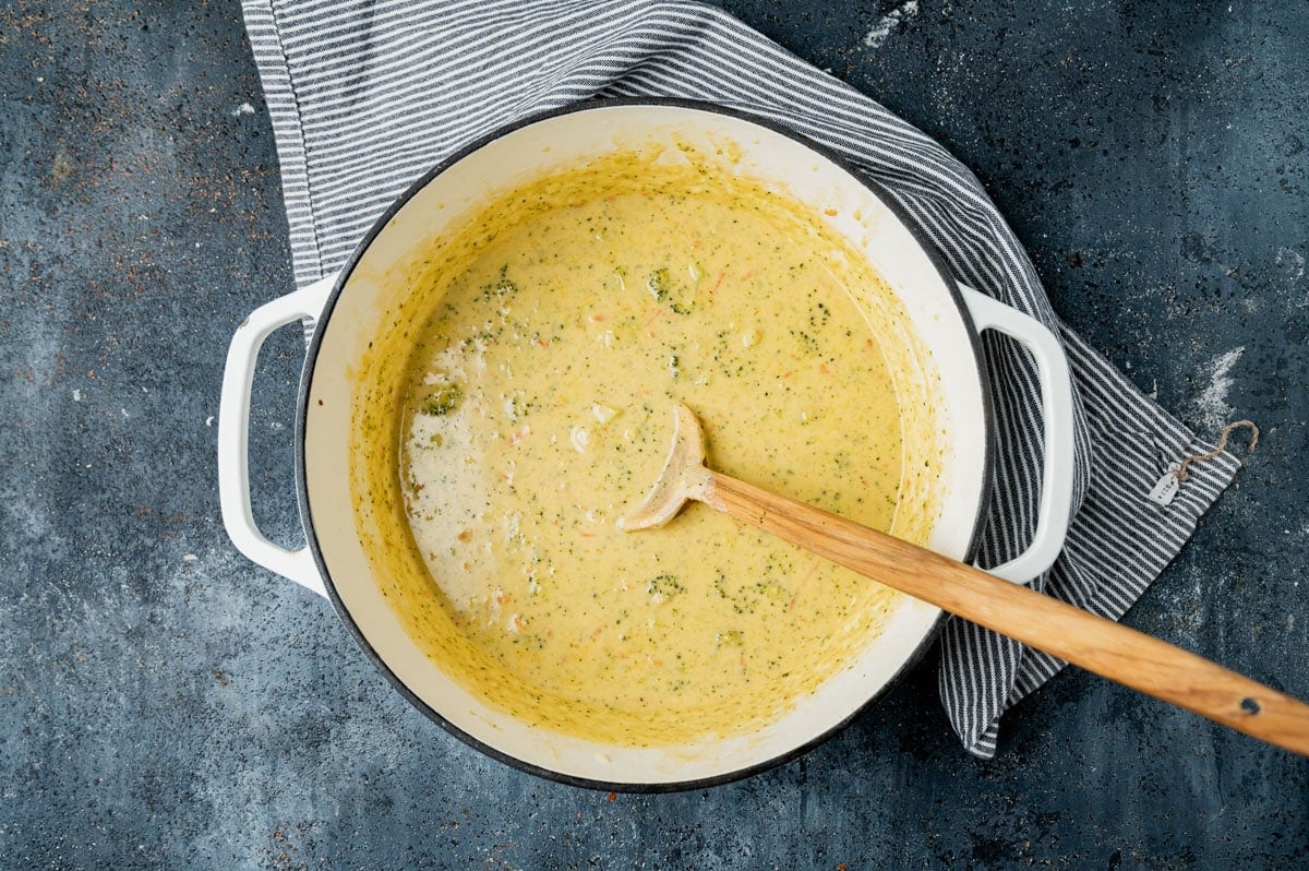 a pan of broccoli cheddar soup with a wooden spoon
