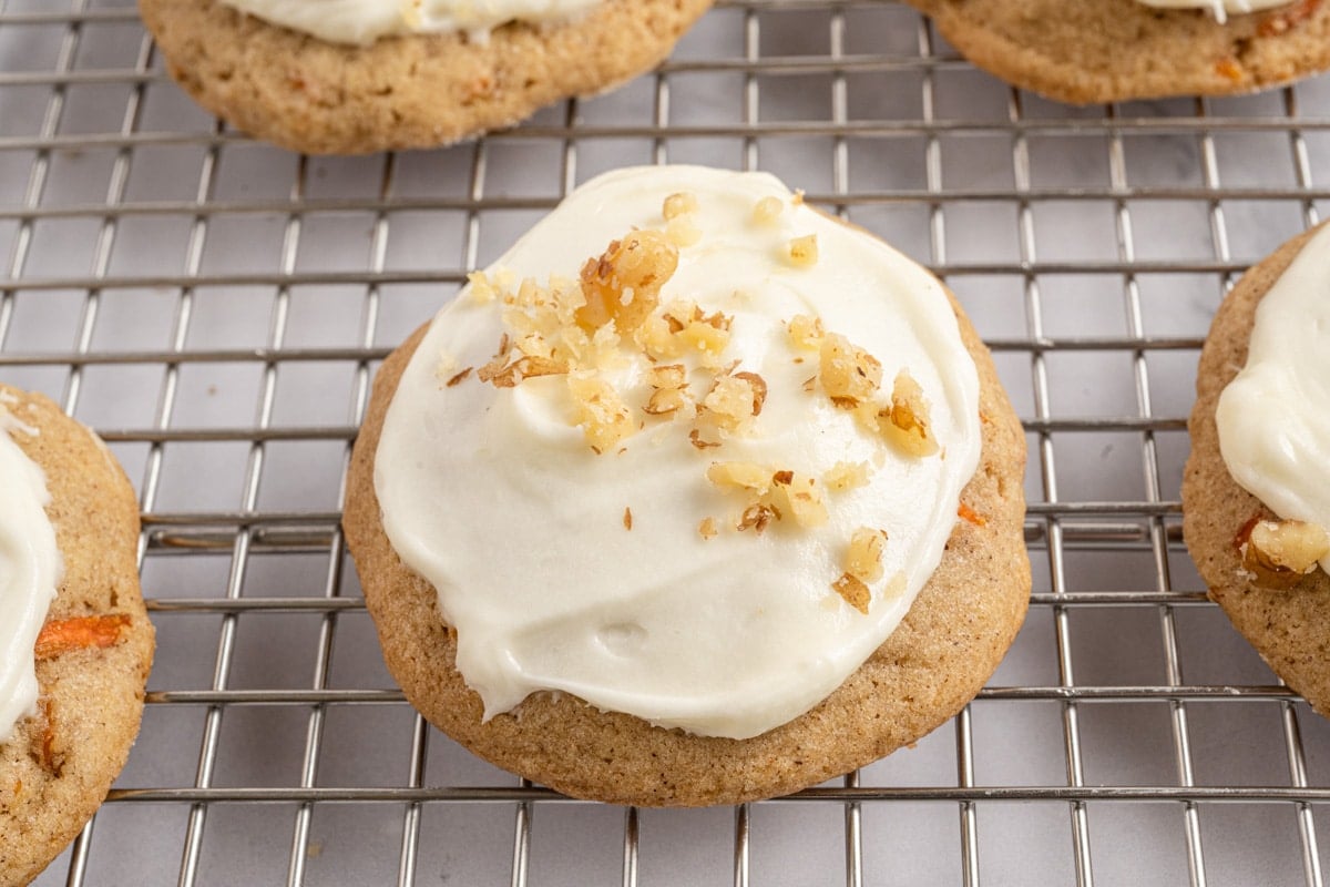 a frosted carrot cookie with walnuts on top on a wire rack