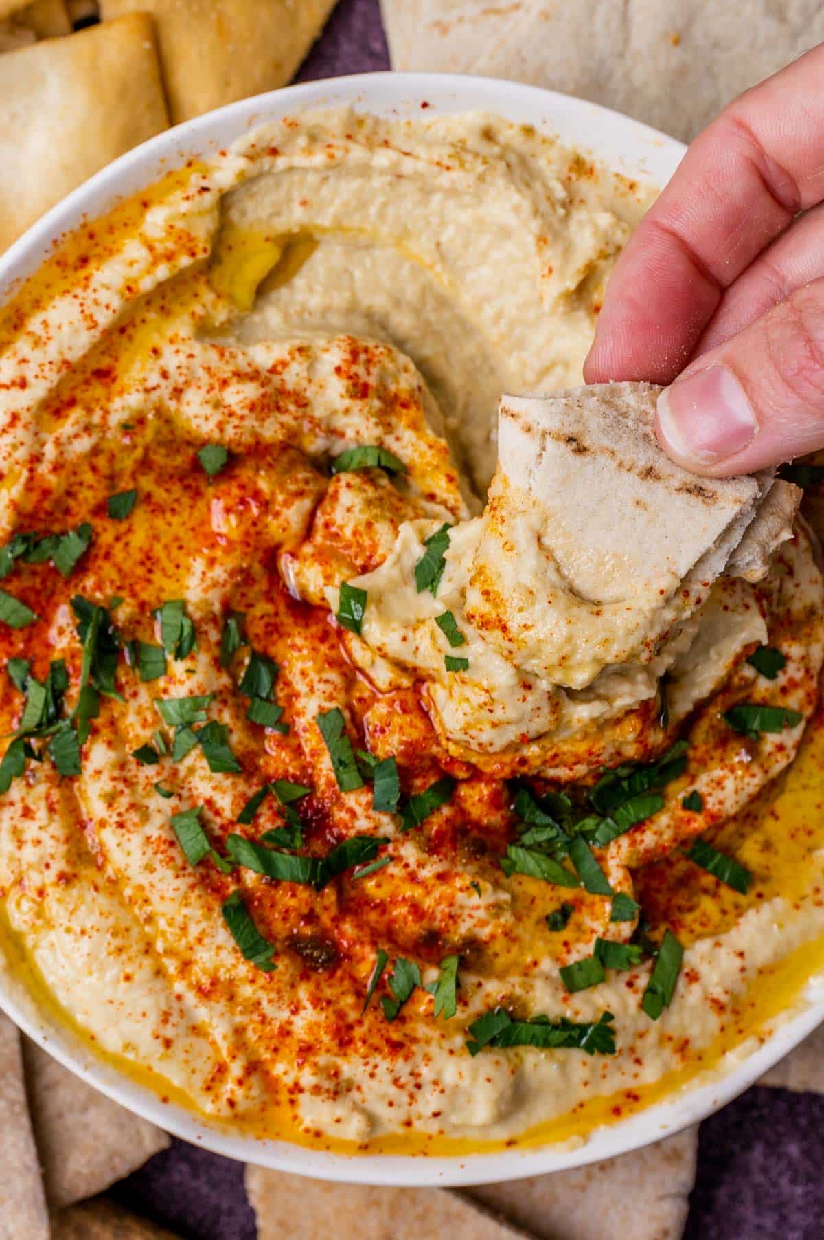 hand dipping pita into creamy hummus