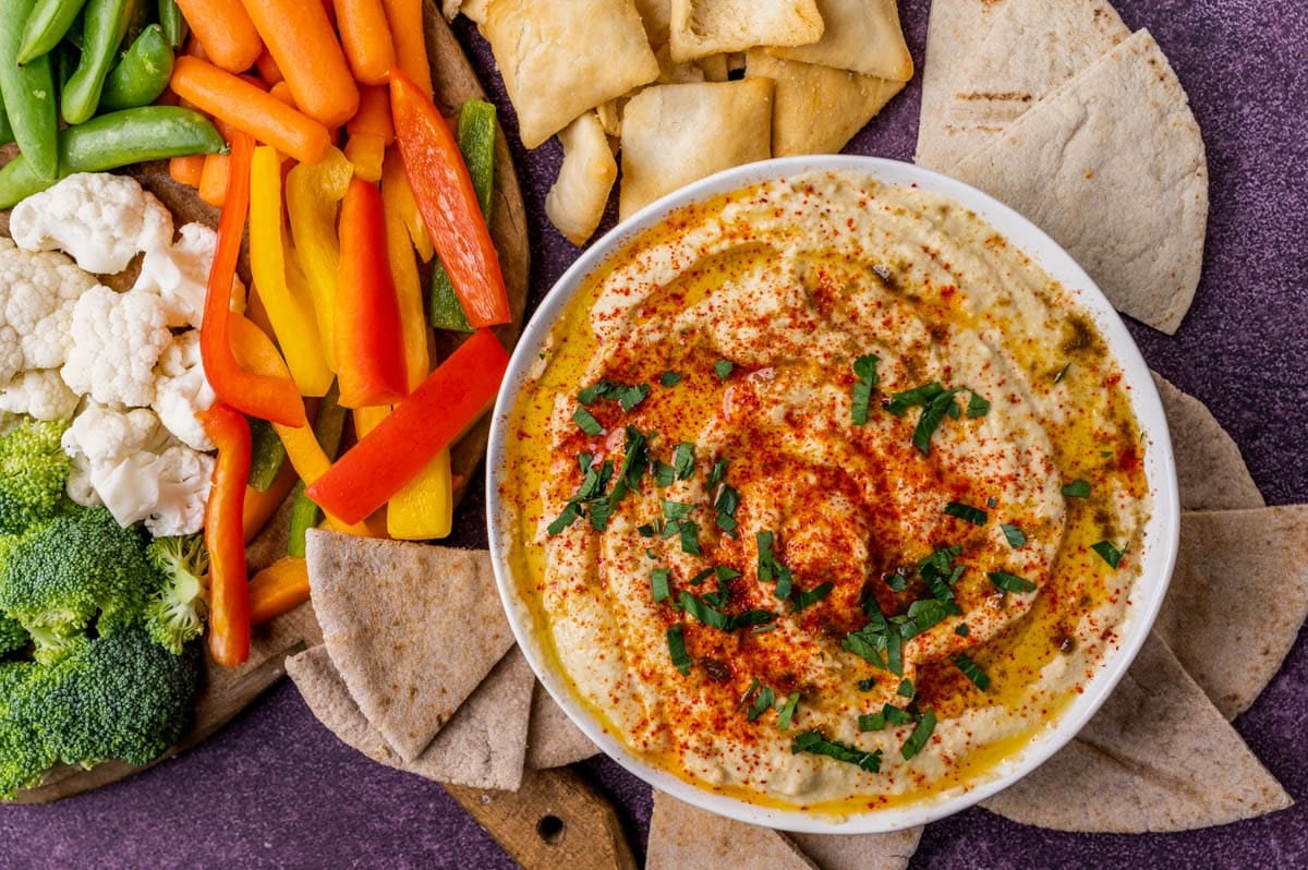 a bowl of hummus on a table with pita and veggies