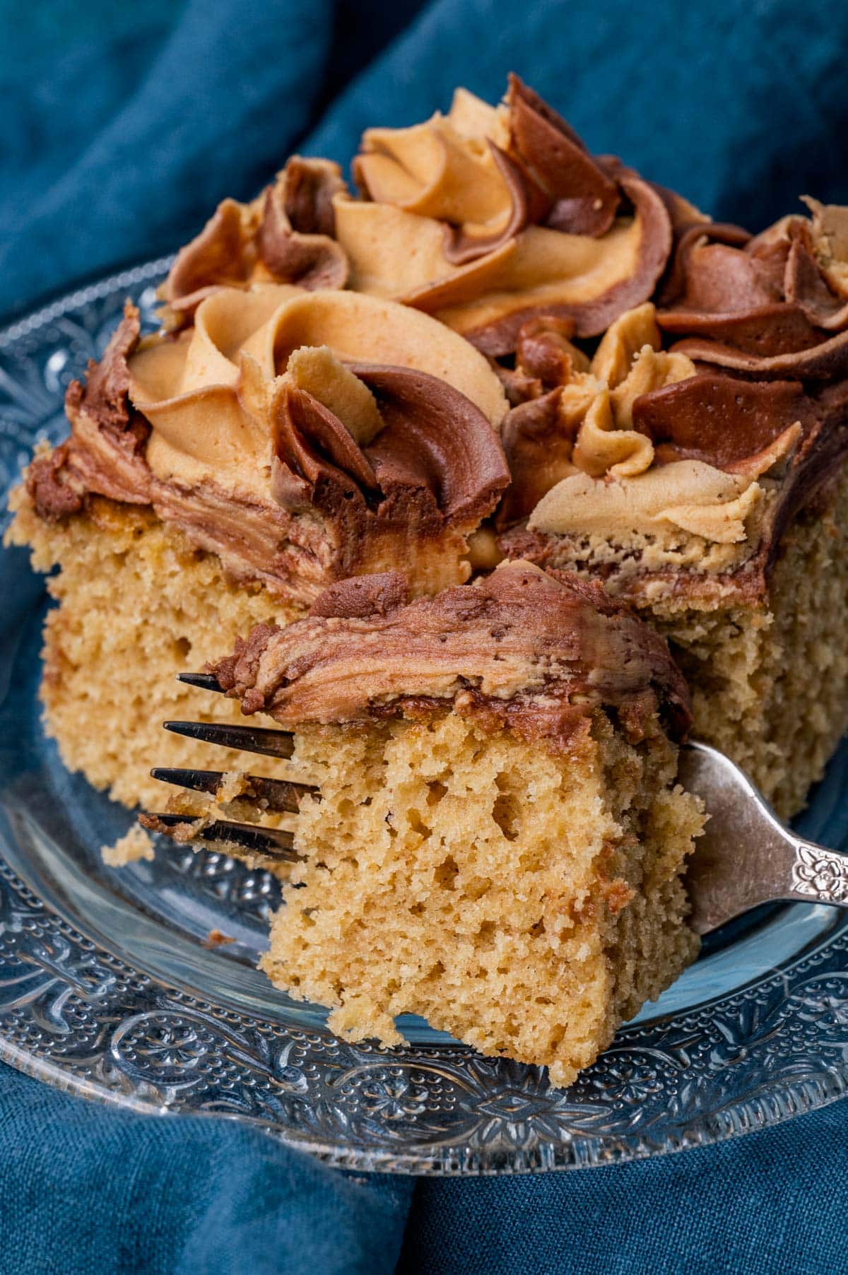 closeup of a piece of peanut butter cake with swirls of frosting on a plate with a fork