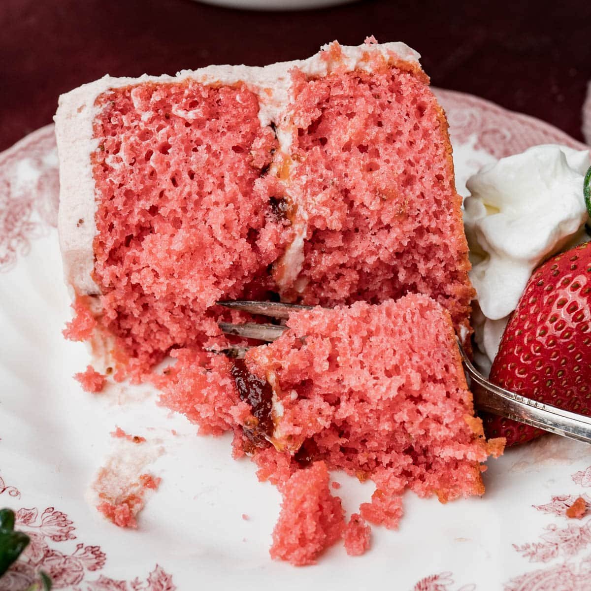 a slice of strawberry layer cake on a plate with a fork and bite out