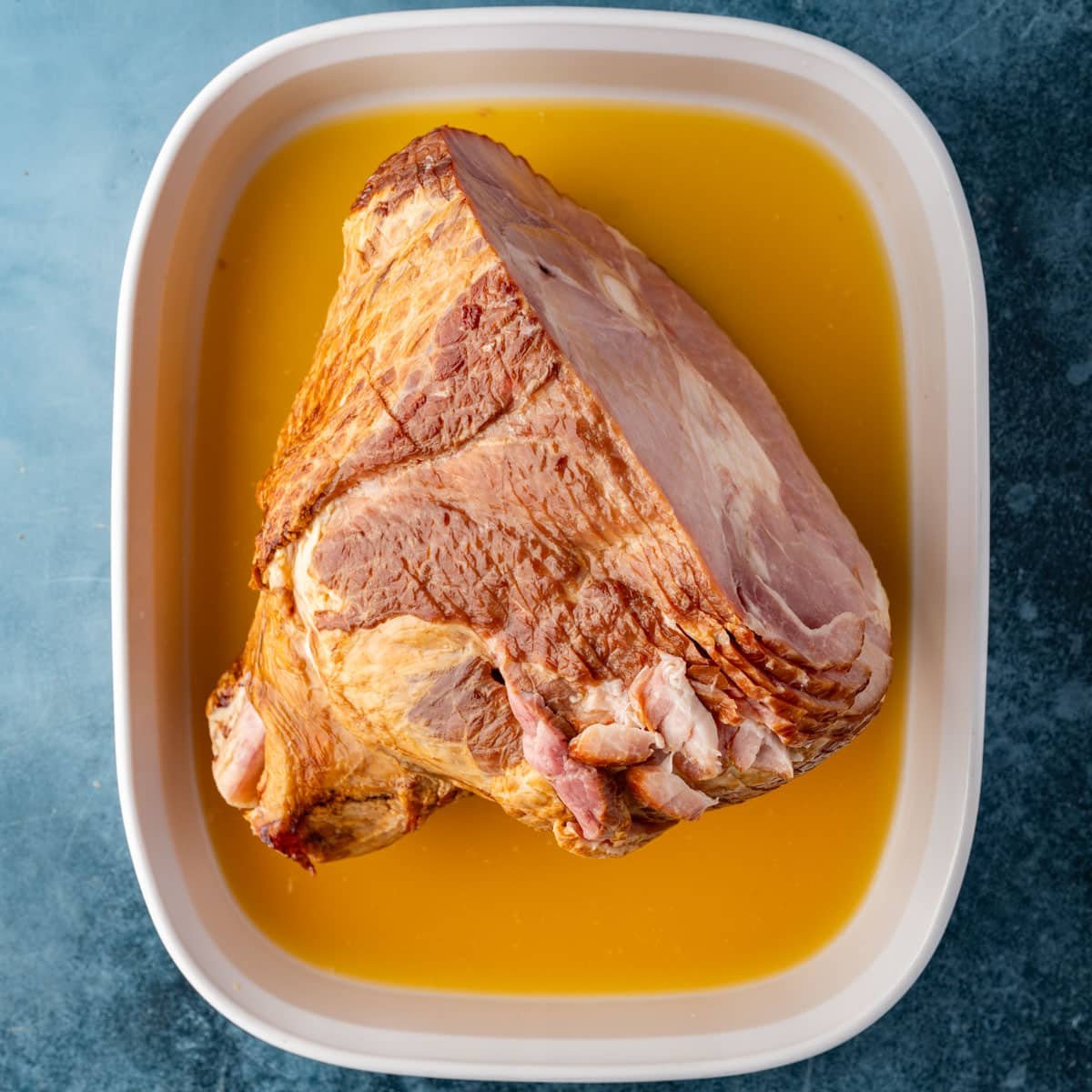 a ham in a roasting pan with orange juice and ginger ale