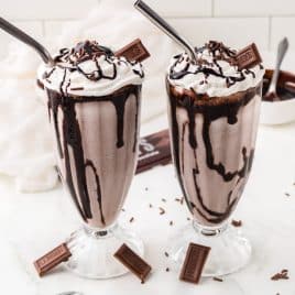 two chocolate milkshakes with straws on a table