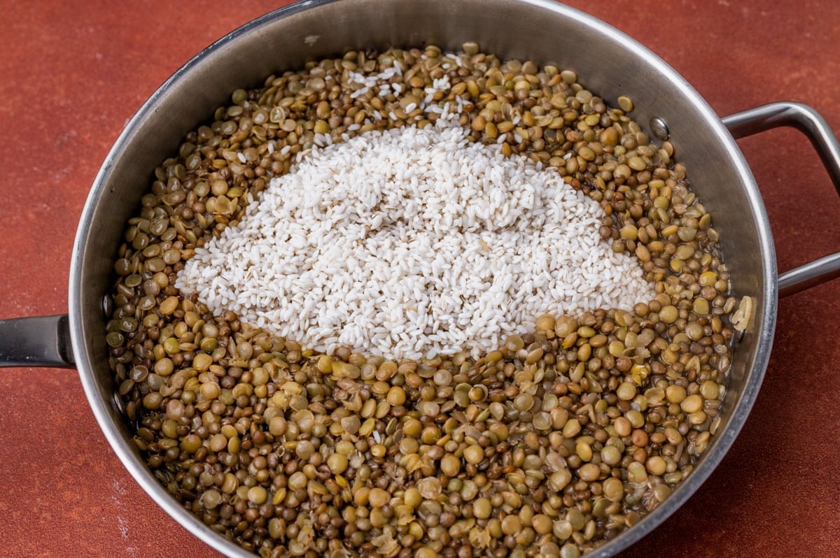 cooked lentils with uncooked rice sitting on top in a skillet