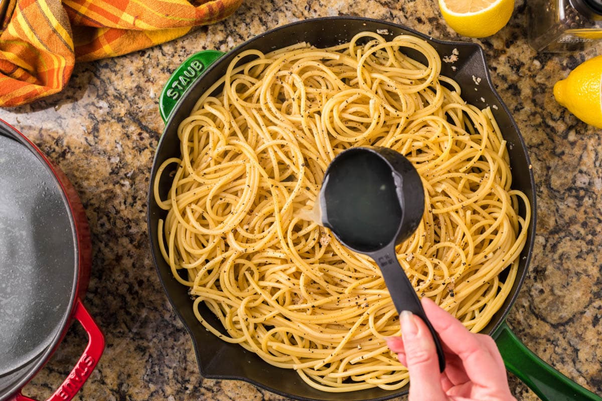pouring pasta water over spaghetti in a skillet