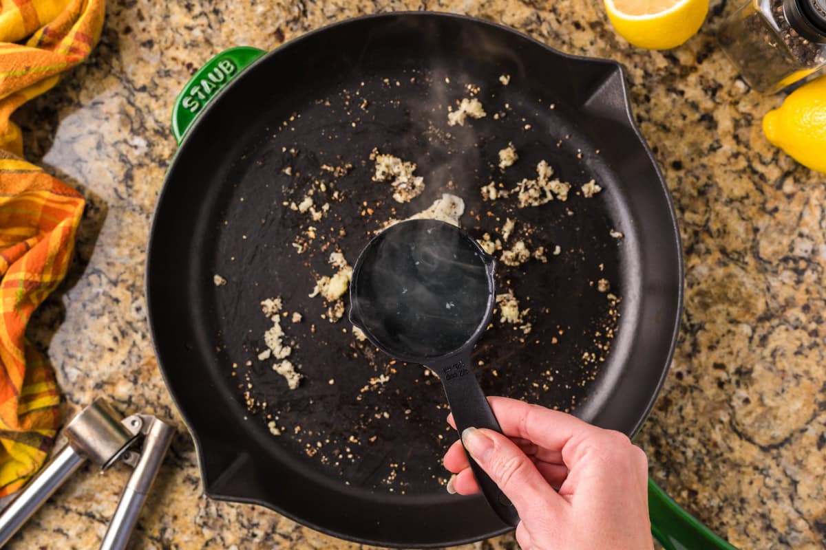 pouring water into skillet with toasted garlic