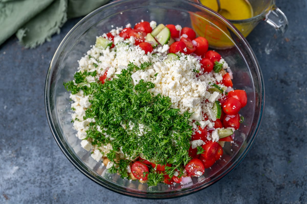 fresh herbs and feta over chickpea pasta salad ingredients in a bowl