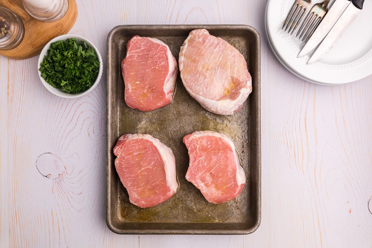 4 plain pork chops on a baking sheet with oil on them