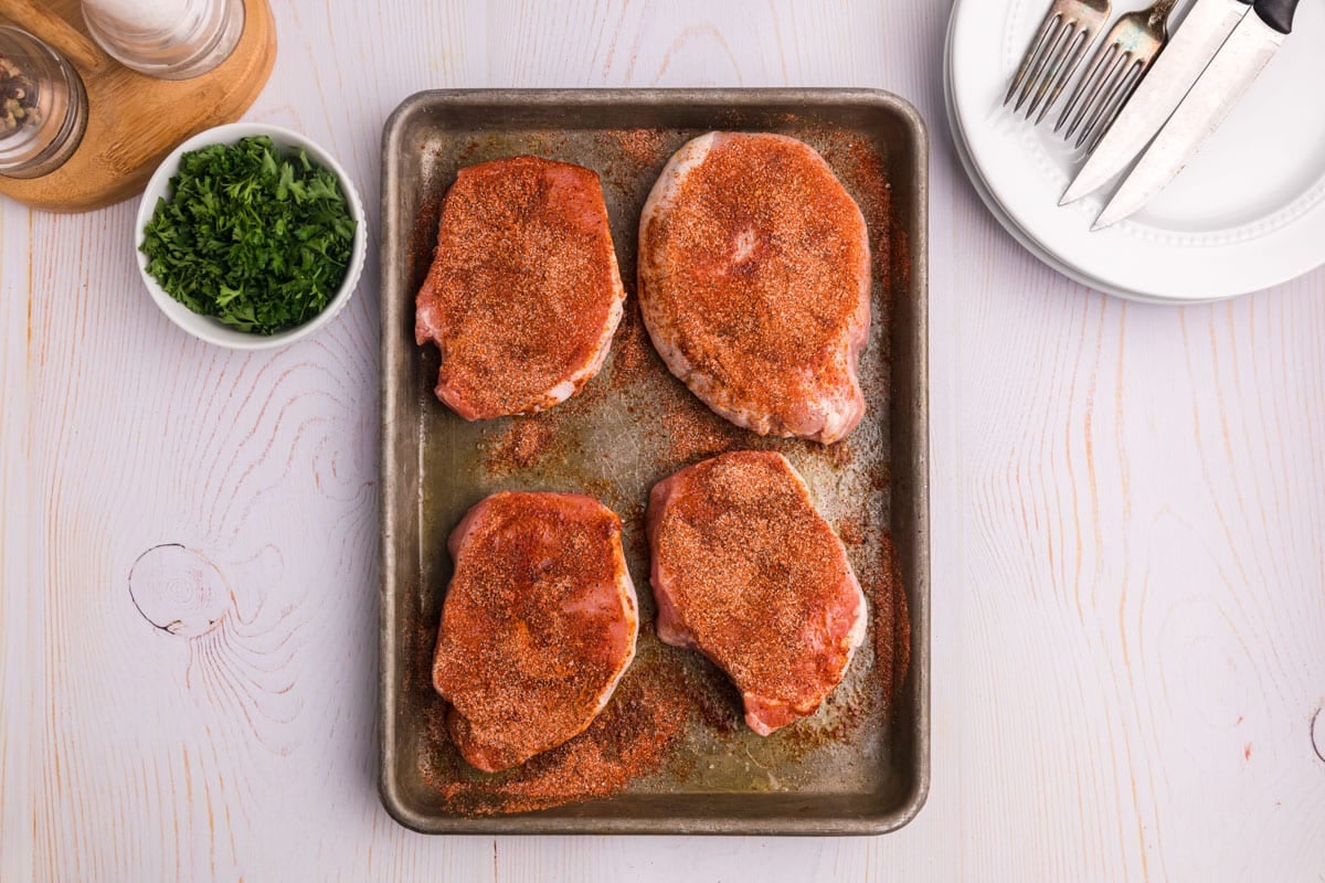 4 seasoned pork chops on a baking sheet