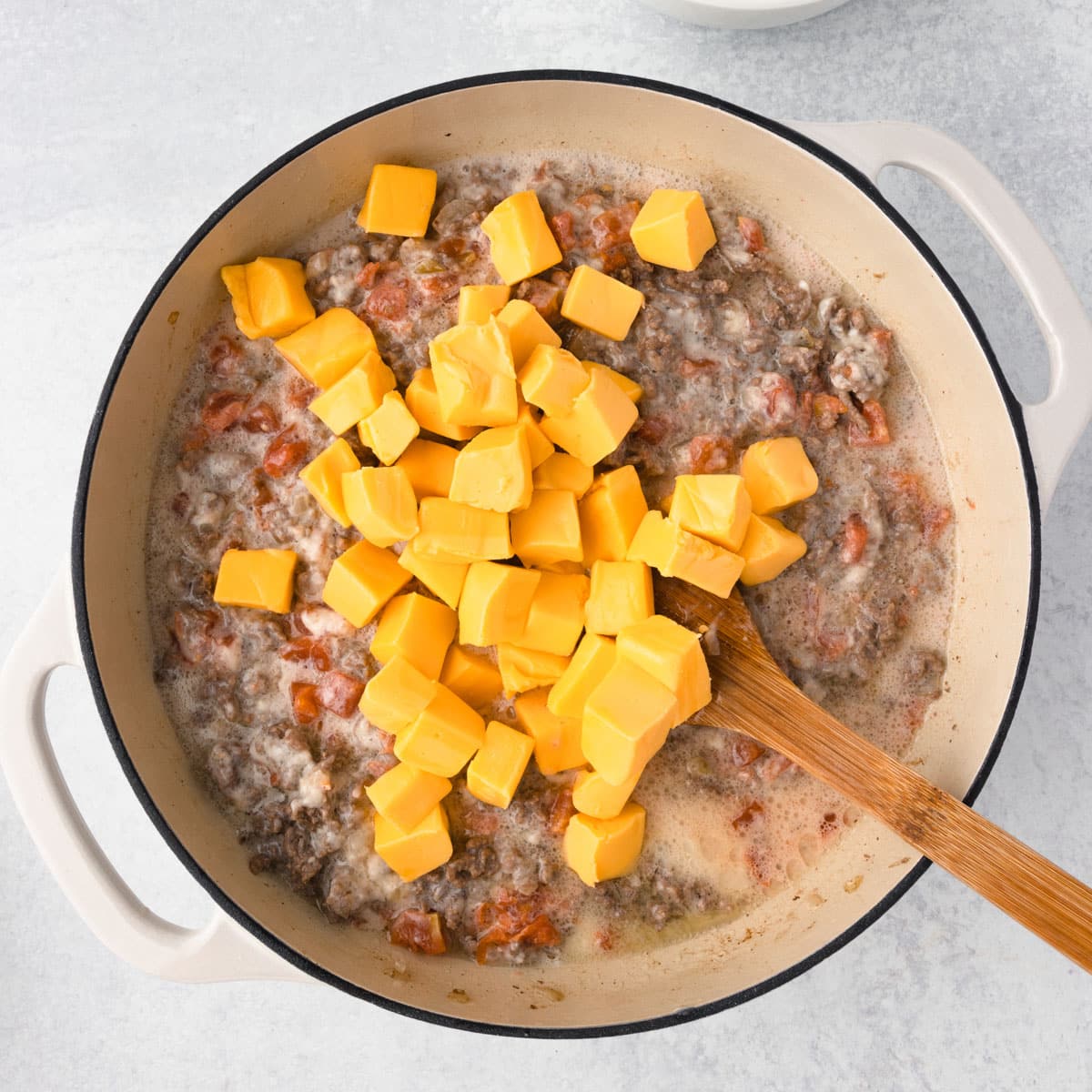 velveeta cubes over ground beef and tomatoes in a skillet