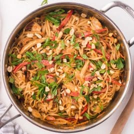 thai peanut noodles in a skillet garnished with red peppers, onions and cilantro