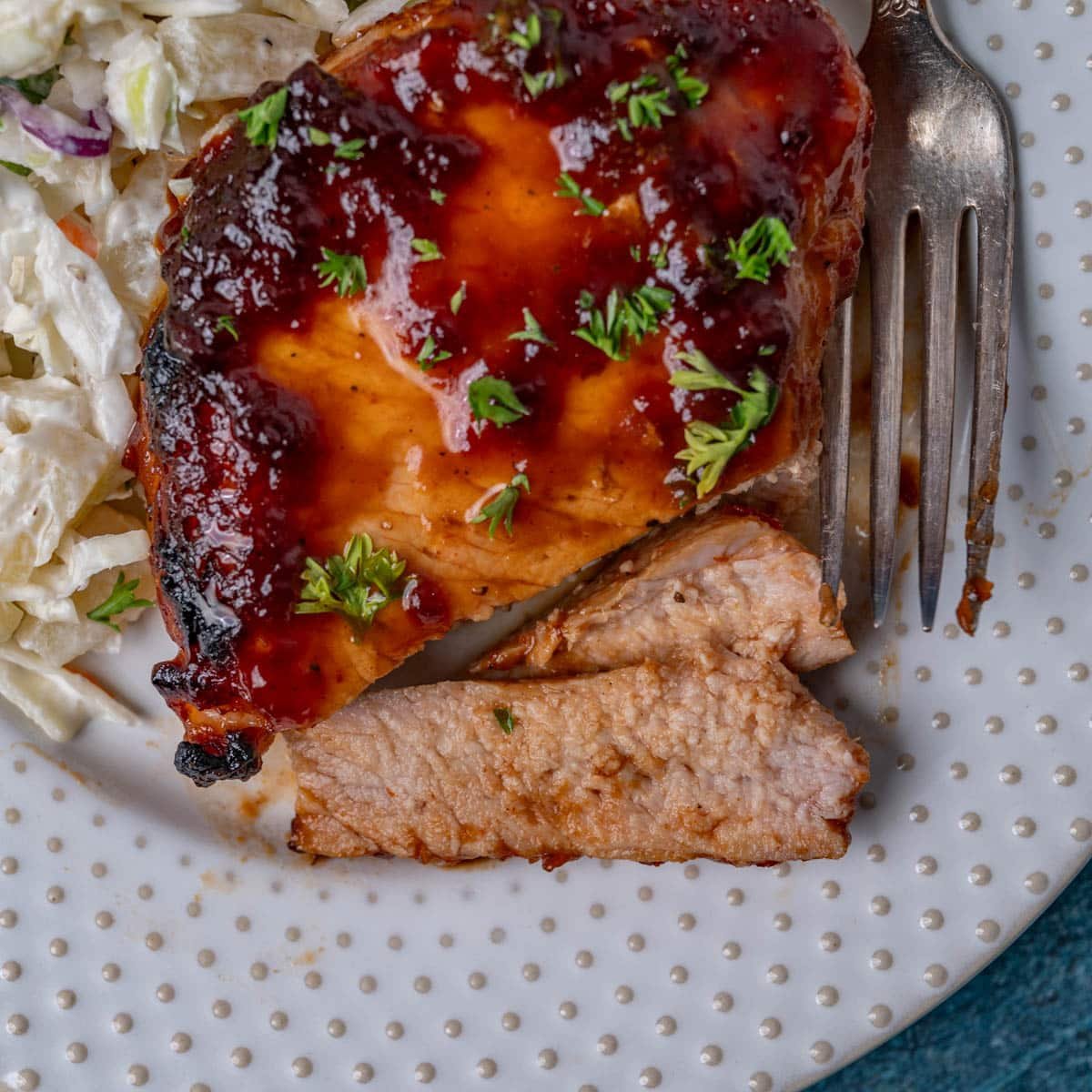 a pork chop with two slices cut off on a plate with a fork