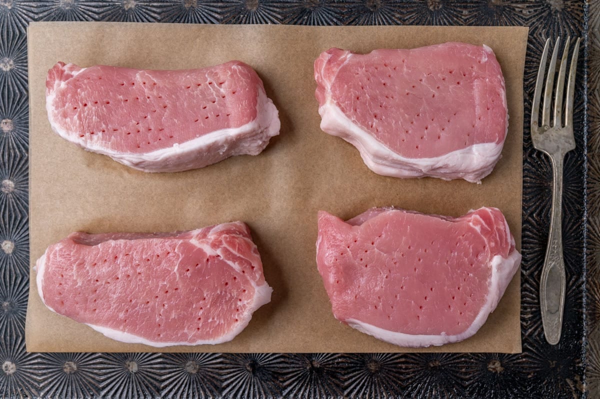 pork chops on parchment paper with fork holes in them