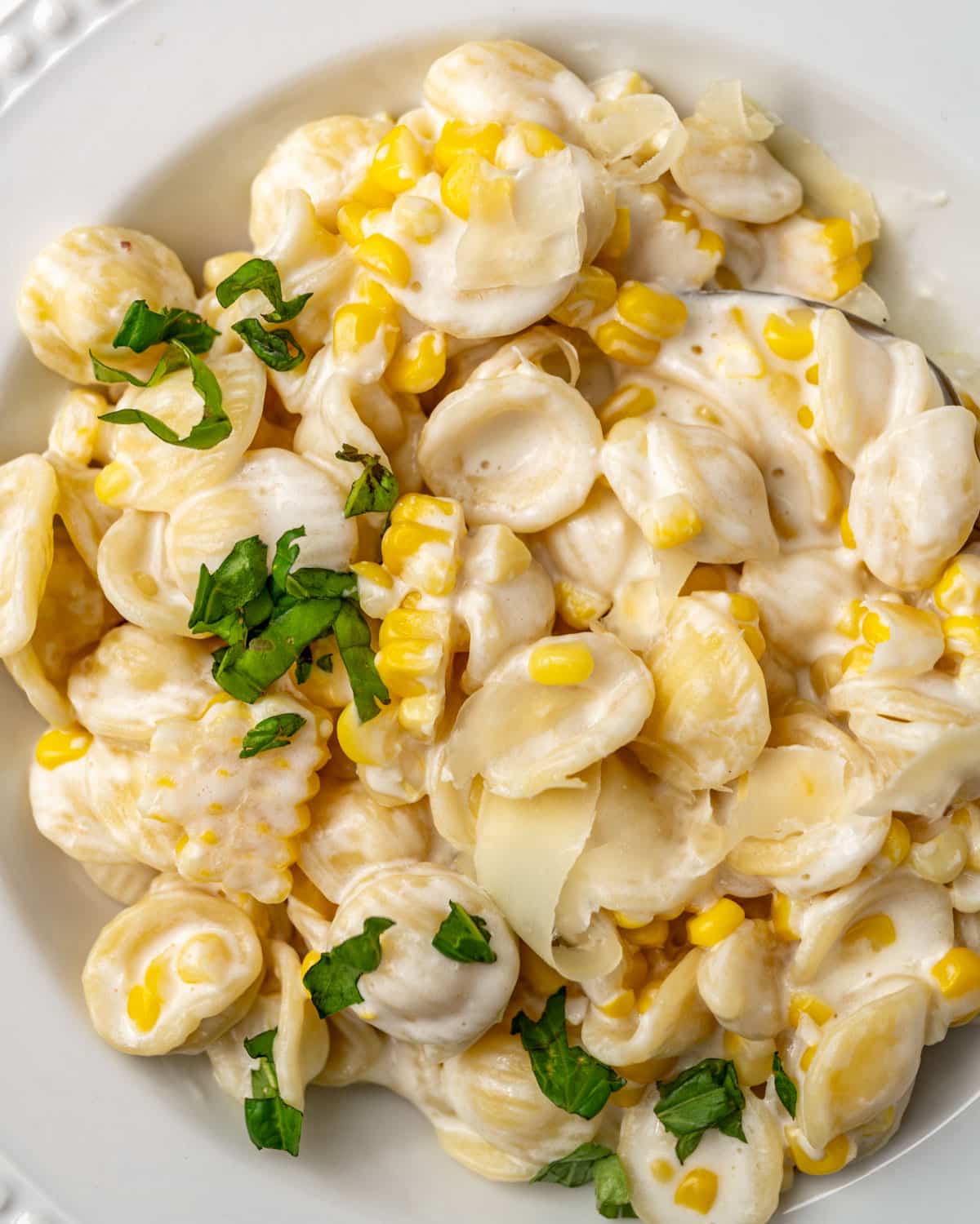 a plate of creamy corn pasta with fresh basil on top