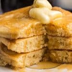 a stack of three griddle cakes with butter and syrup with one bite cut out