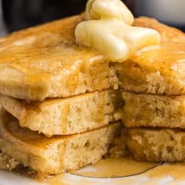 a stack of three griddle cakes with butter and syrup with one bite cut out