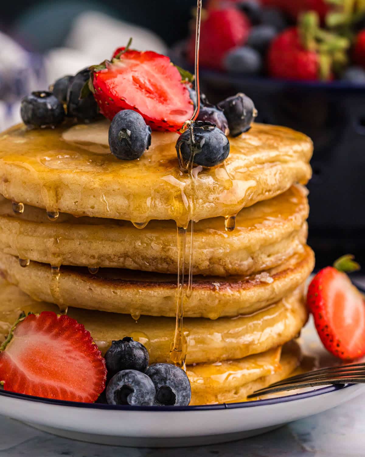 a stack of griddle cakes with fresh fruit and syrup