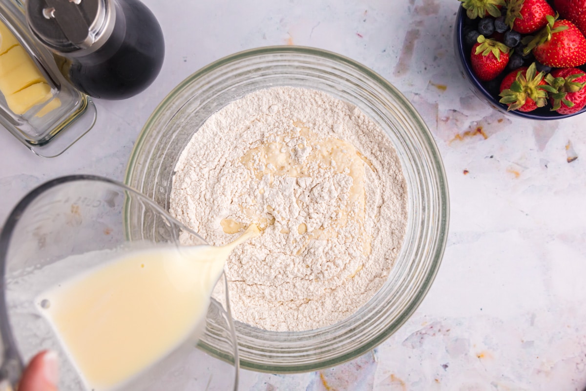 milk pouring into dry ingredients in a glass bowl