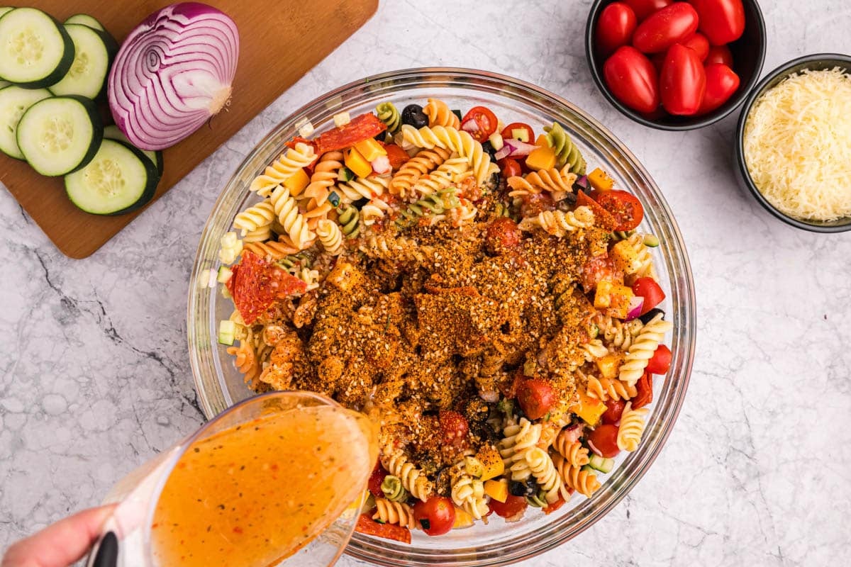 pouring Italian dressing over pasta salad in a bowl