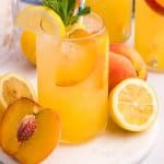 a glass of peach lemonade on a table with lemons and peaches