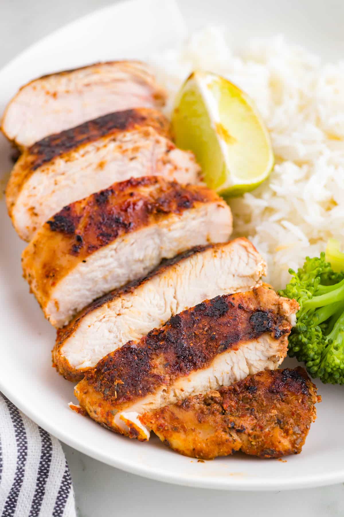 a piece of blackened chicken on a plate with rice and broccoli