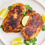 a plate of two chicken breasts with seasoning