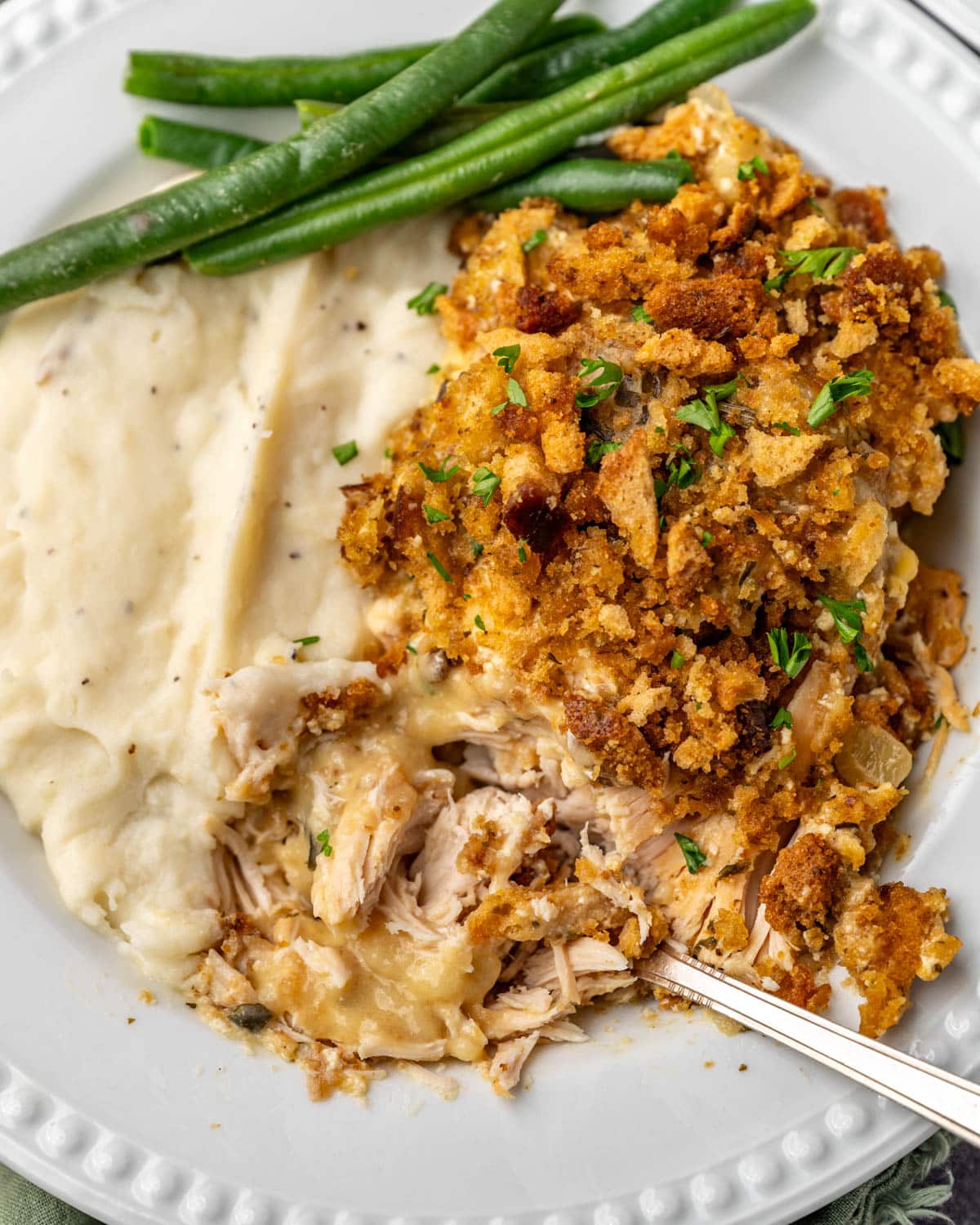 a plate of chicken and stuffing with mashed potatoes and green beans with a fork