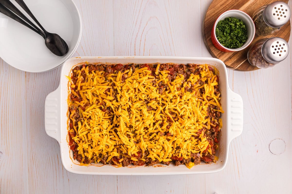 unbaked johnny marzetti casserole with shredded cheddar cheese on top