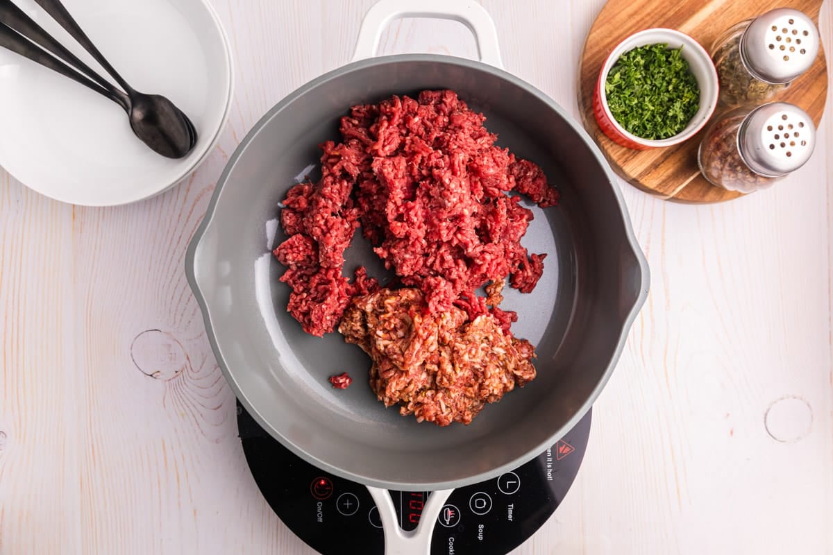 ground beef and sausage uncooked in a skillet