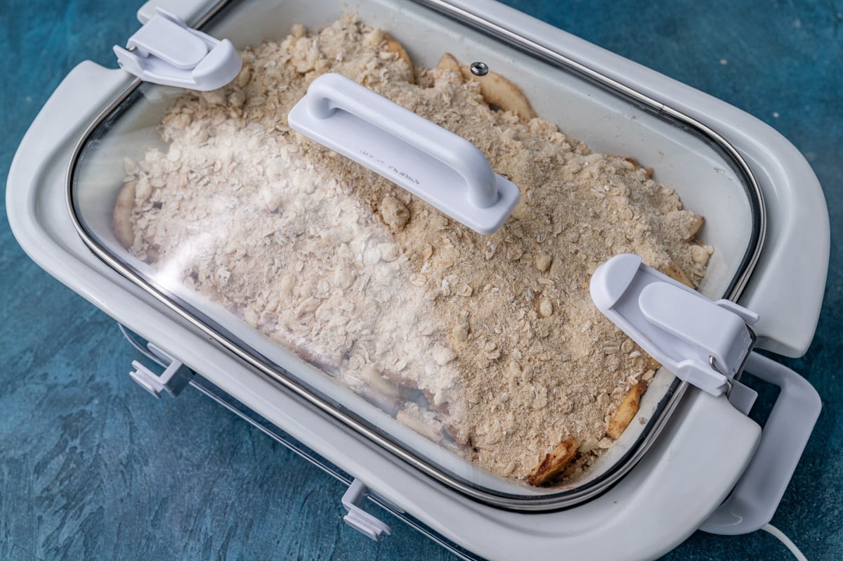 uncooked apple crisp in a slow cooker with a lid on it