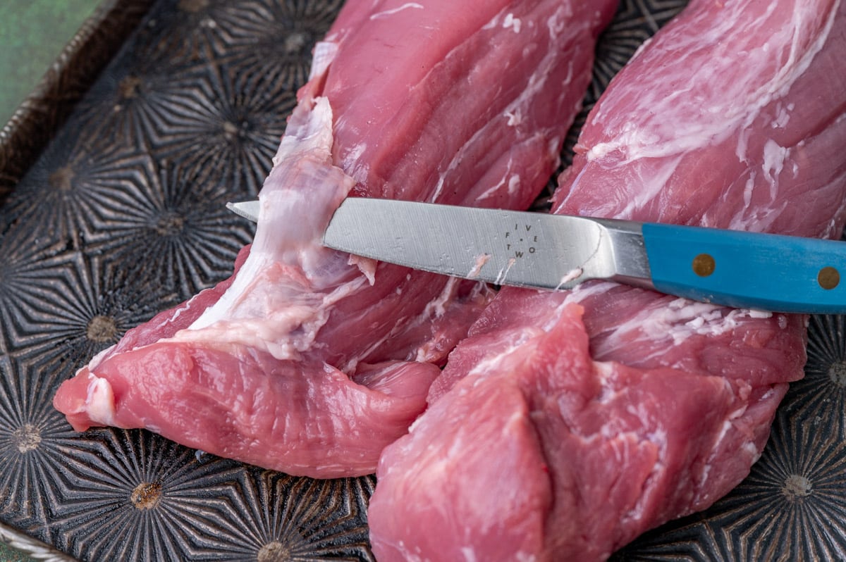 a knife cutting the silverskin off of pork loin