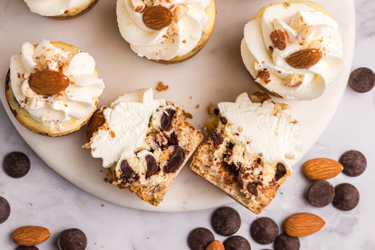 overhead view of mini almond chocolate chip cheesecakes on a plate, with one cut in half