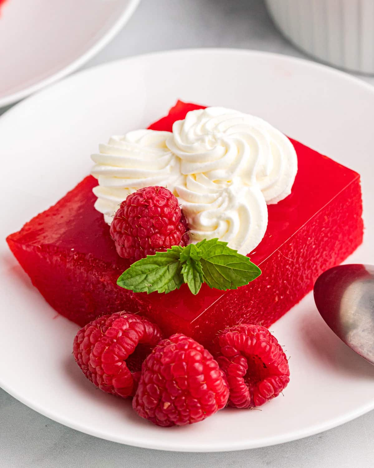 applesauce jello on a plate with whipped cream, fresh raspberries and mint