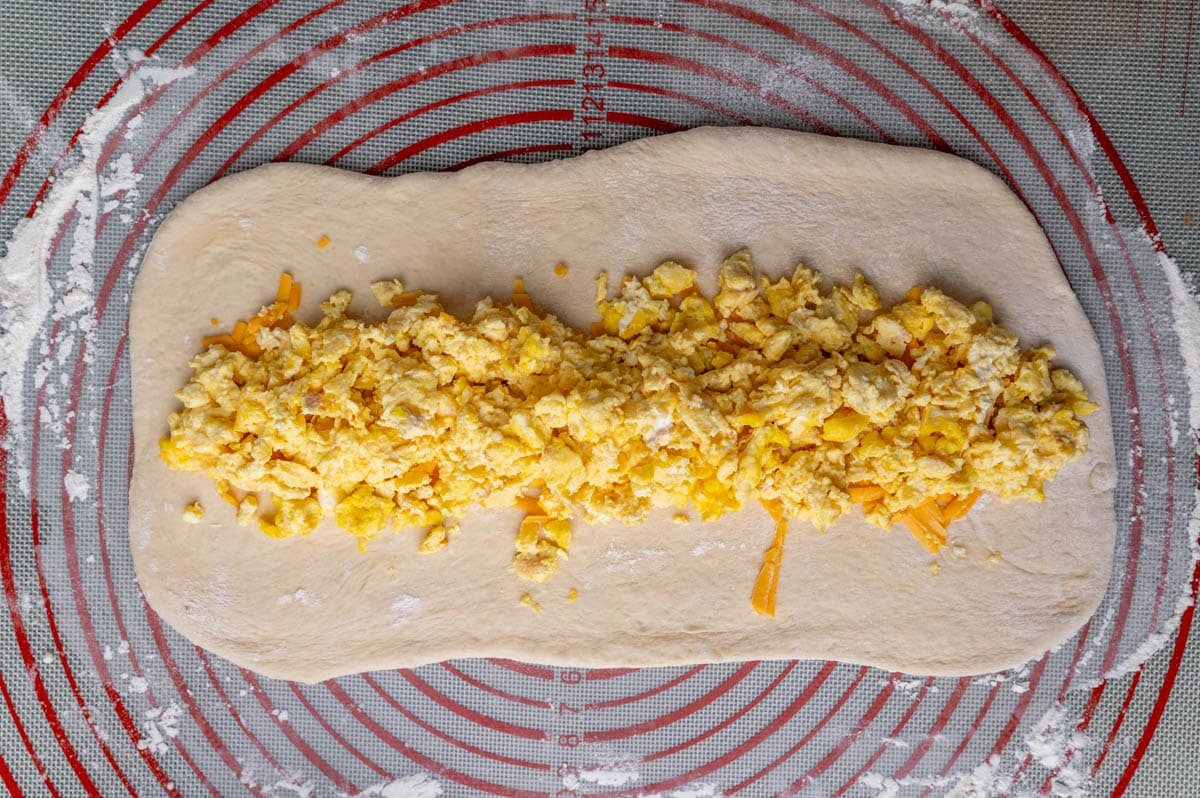 bread dough rolled out with scrambled eggs and cheese on top