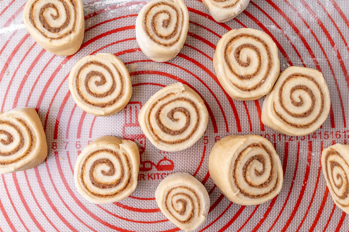 cinnamon roll dough cut into rolls on a pastry mat